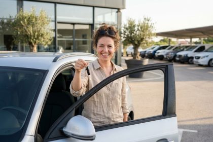 Femme souriante récupérant une voiture automatique de location devant une agence de location de voitures